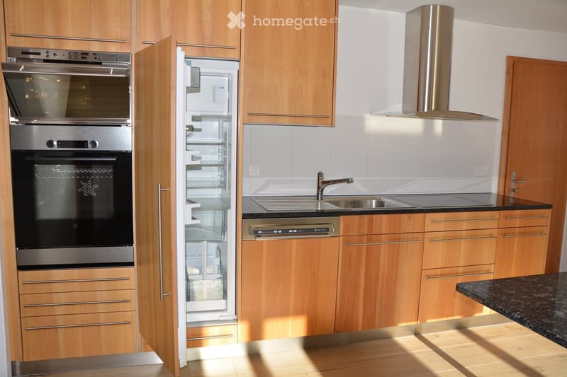 Modern kitchen with wooden cabinets, stainless steel appliances including an oven, refrigerator, and range hood, and a granite countertop.
