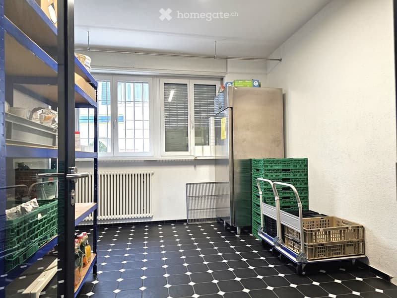 A storage or utility room with black and white tiled floor, metal shelves, refrigerator, and green crates stacked on a cart.