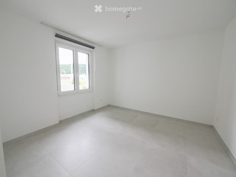 Empty room with white walls, tiled floor, and large window with blinds.