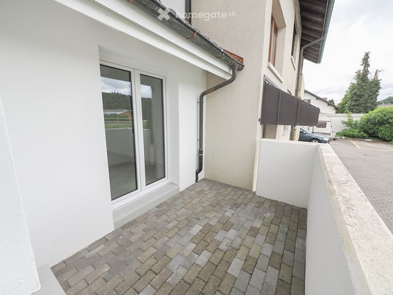 Balcony with brick paving, large window, and white walls.