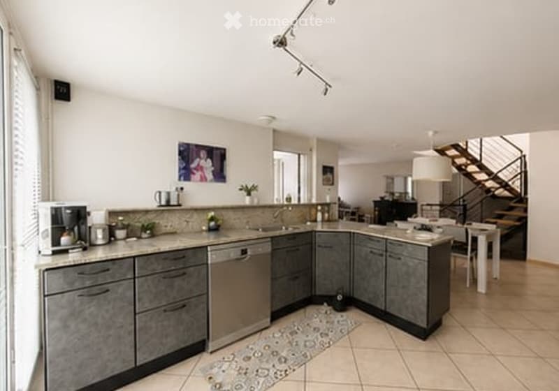 Modern kitchen with grey cabinets, stainless steel appliances, a coffee maker, sink, and a small dining area with a table and chairs.