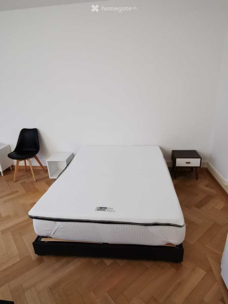 Minimalist bedroom with a single bed, a black chair, and a small nightstand.