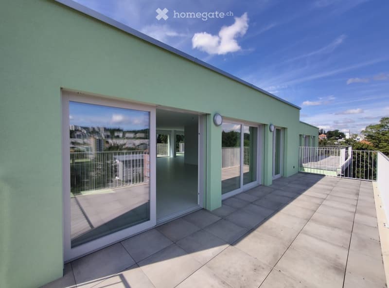 A modern balcony with tiled flooring, glass sliding doors, and metal railings, offering a view of the cityscape.