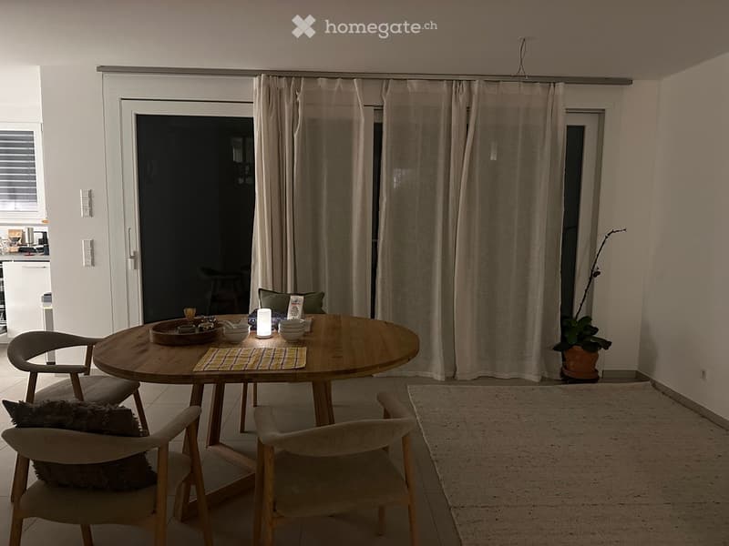 A modern dining area with a round wooden table, four chairs, a lamp, and a potted plant near the window.