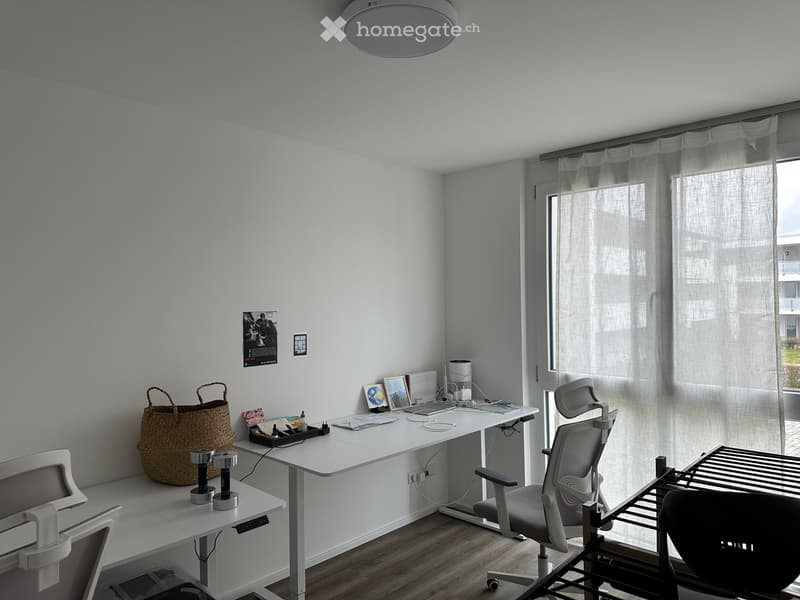 Modern, minimalist office space with a white desk, ergonomic chair, laptop, and decorative items including a woven basket and picture frames.