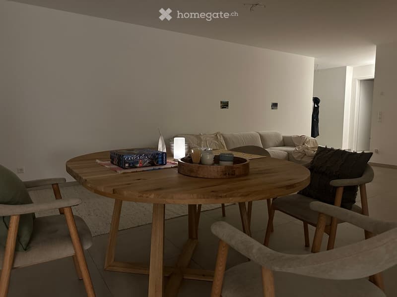 Modern living room with a round wooden coffee table, sofa, chairs, and decorative items including a board game and a tray with cups.
