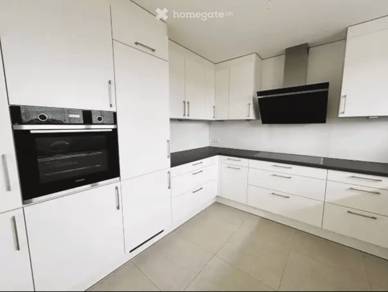 Modern kitchen with white cabinets, black countertops, and stainless steel appliances including an oven and range hood.