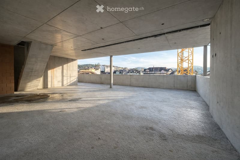 Empty concrete space with a raised ground floor, exposed beams, and a view of the surrounding area through an open side.