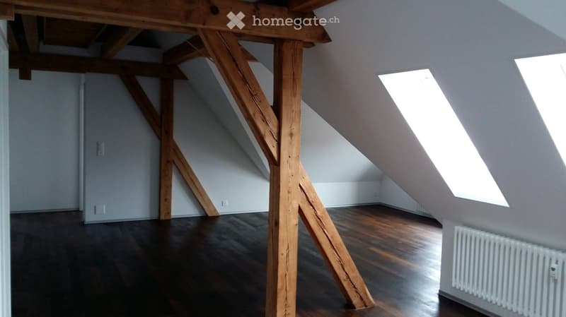Unfurnished Room. Empty attic space with wooden beams, wooden flooring, and skylight windows.