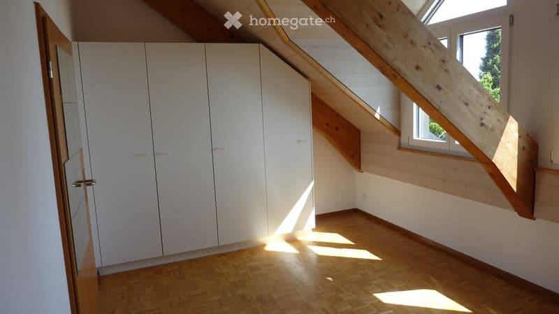 Empty room with wooden flooring, white walls, built-in white closet, and a wooden staircase leading to an upper level with a skylight window.