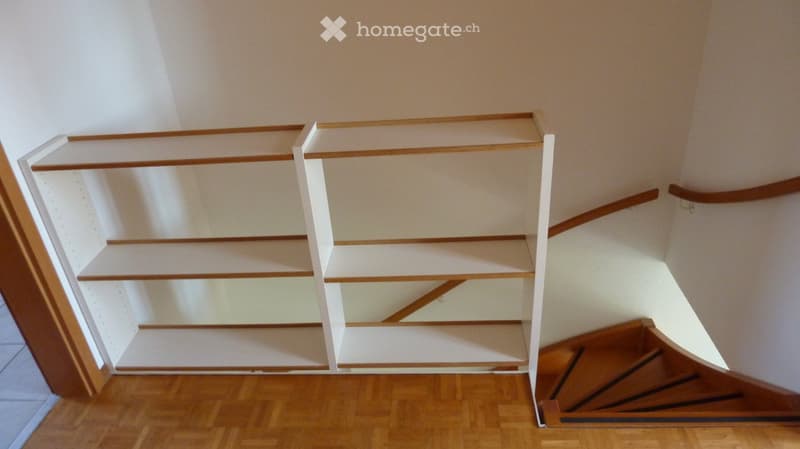 Empty hallway with wooden floor, white walls, and built-in shelving unit with wooden trim and white panels.