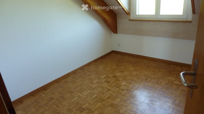 Empty room with wooden herringbone flooring, white walls, and a window with wooden frame. No furniture or equipment present.