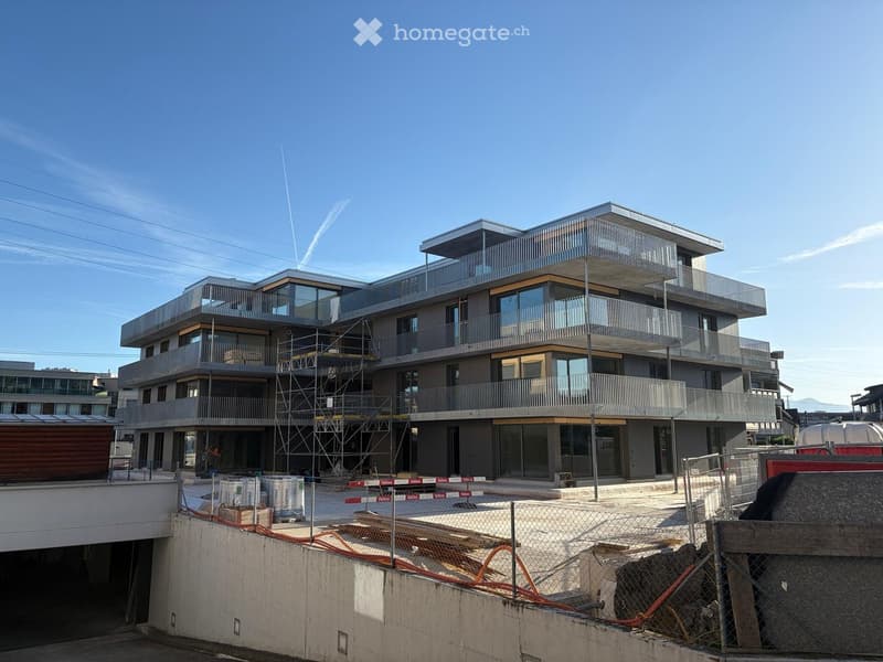 Modern multi-story residential building with balconies, large windows, and a contemporary design, under construction with scaffolding and fencing.
