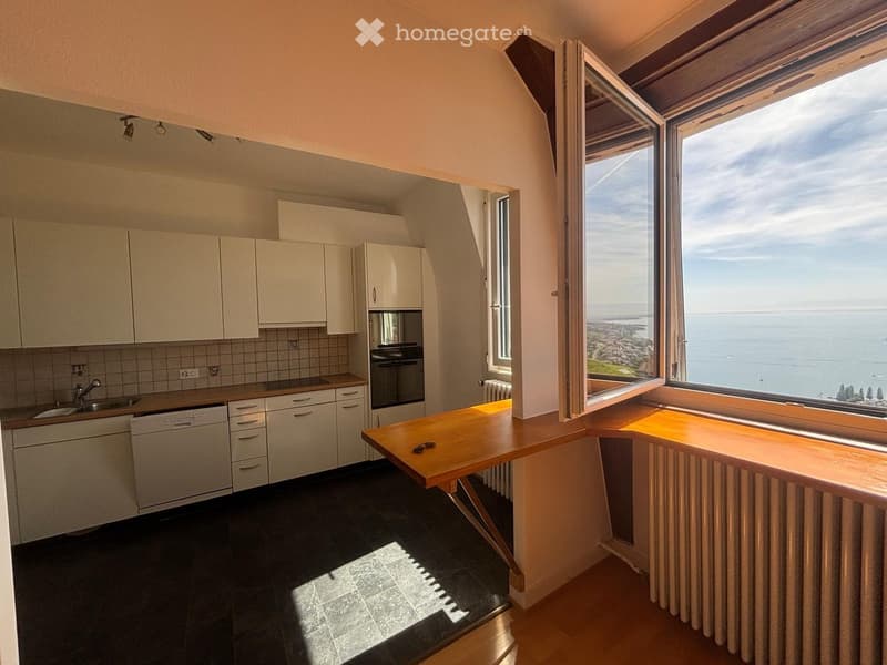 Modern kitchen with white cabinets, stainless steel appliances, and a large window offering a scenic ocean view.