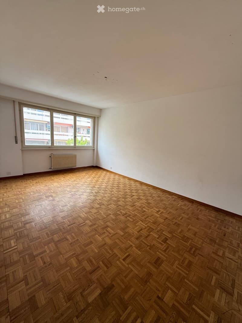 Empty room with wooden herringbone flooring, white walls, and large windows with a radiator below. No furniture or equipment present.