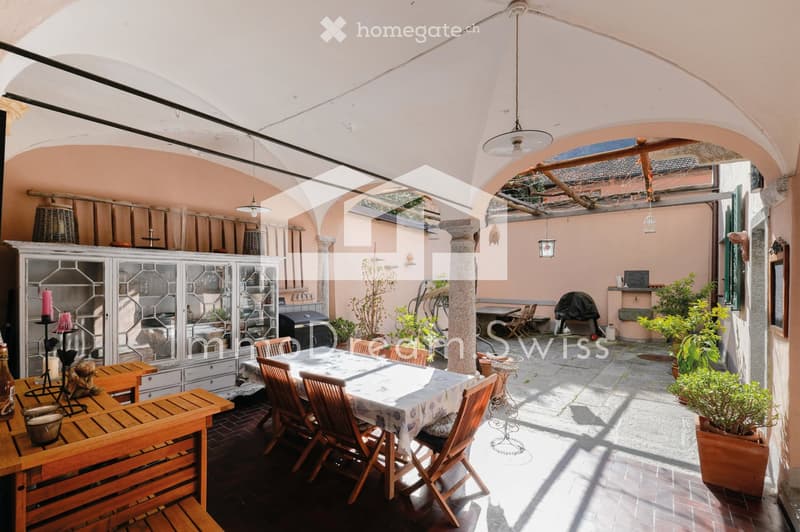 Courtyard with wooden furniture, dining table, chairs, potted plants, and a covered seating area with hanging lights.