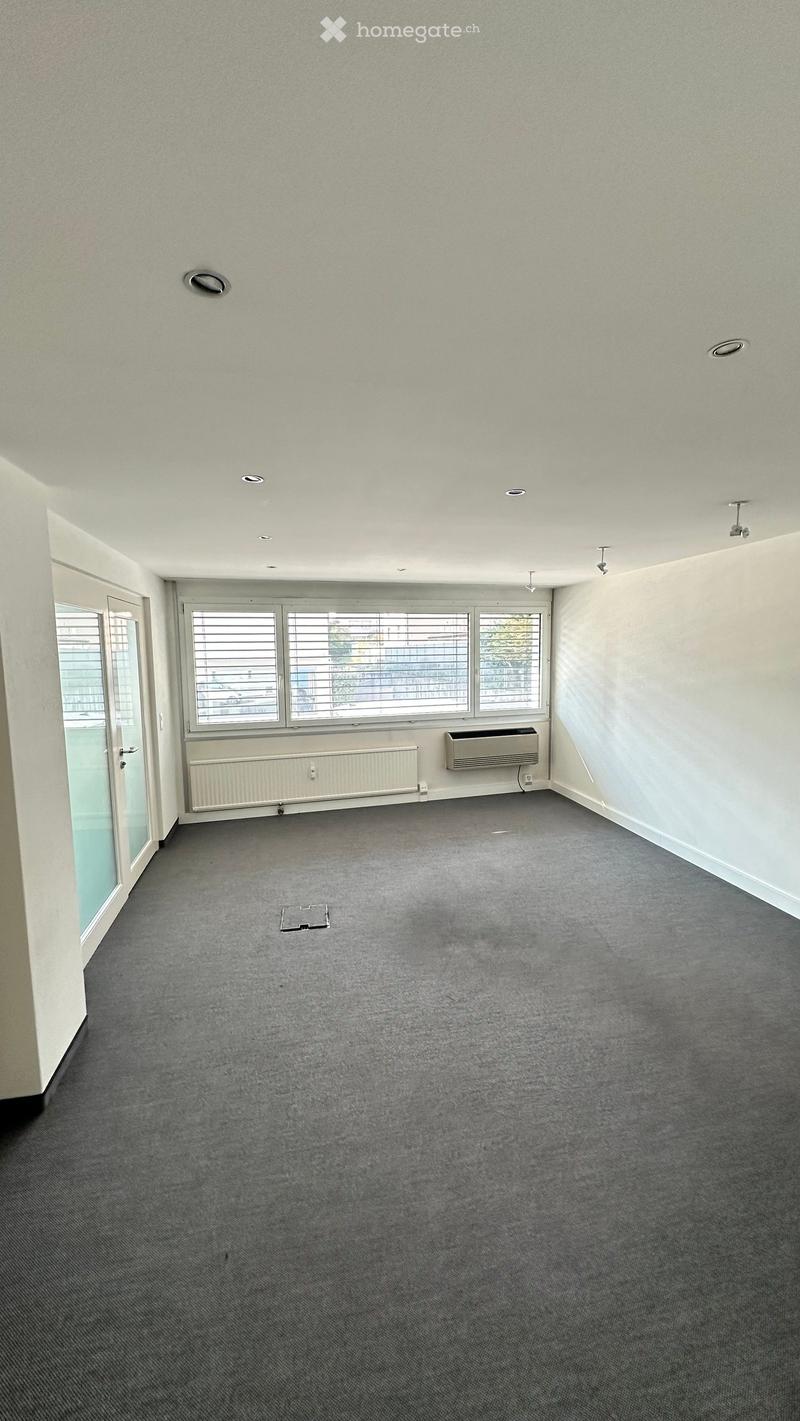 Empty room with grey carpet, white walls, large windows with blinds, and a door leading outside. No furniture or equipment present.