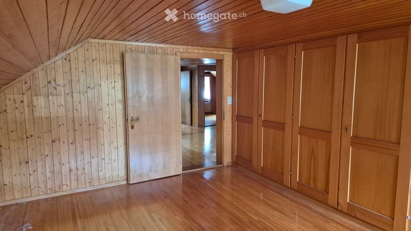 Empty room with wooden walls and floor, featuring a door leading to another room.