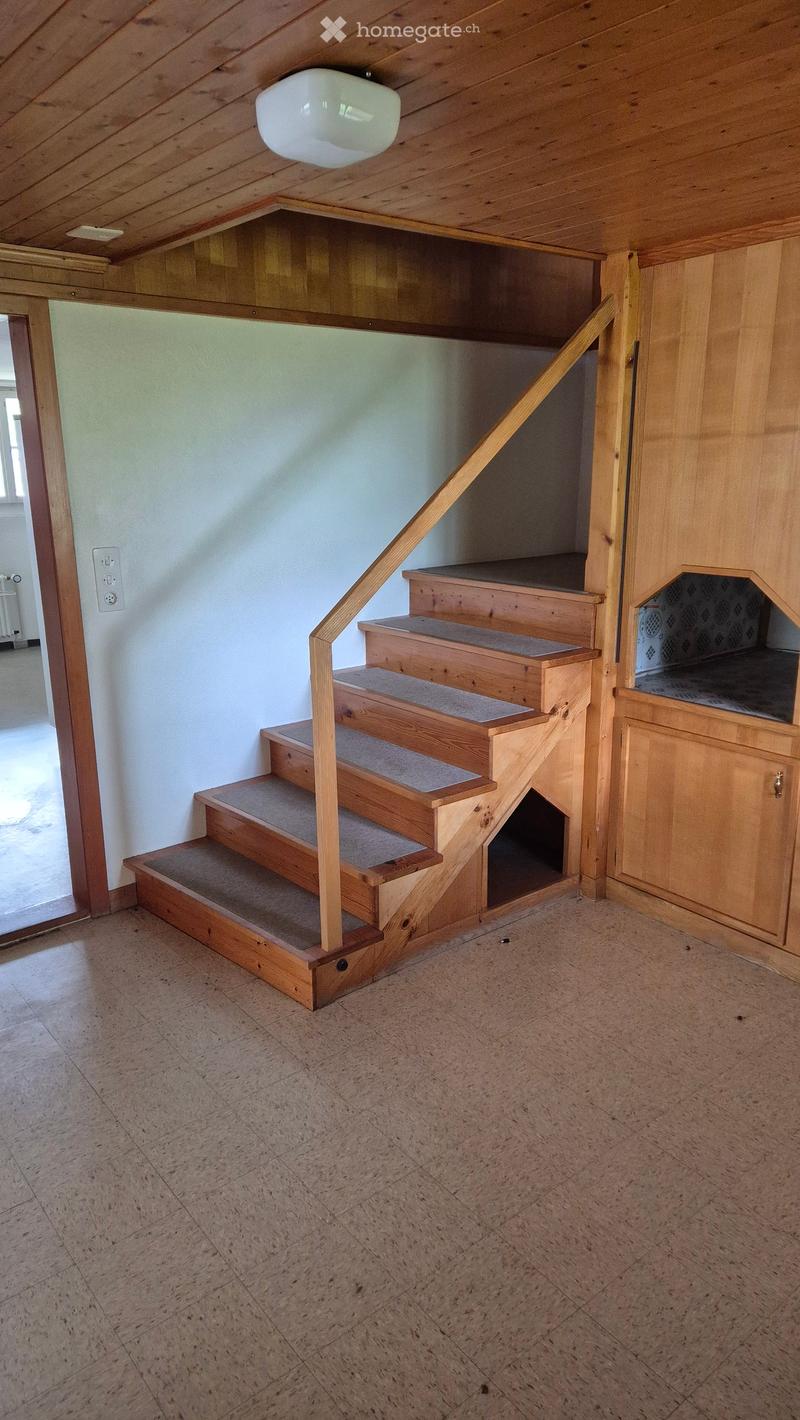 Wooden staircase with carpeted steps, wooden handrail, and built-in storage cabinet on the right side. The ceiling has exposed wooden beams and a single light fixture.