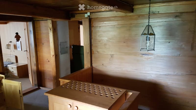 A rustic wooden room with a table, cabinet, hanging lantern, picture frame, and chair.