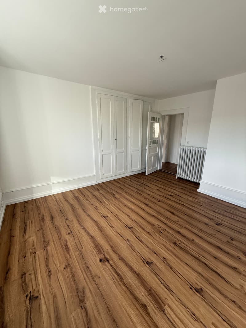 Empty room with wooden flooring, white walls, and built-in white closet units. A radiator is visible in the adjacent room.