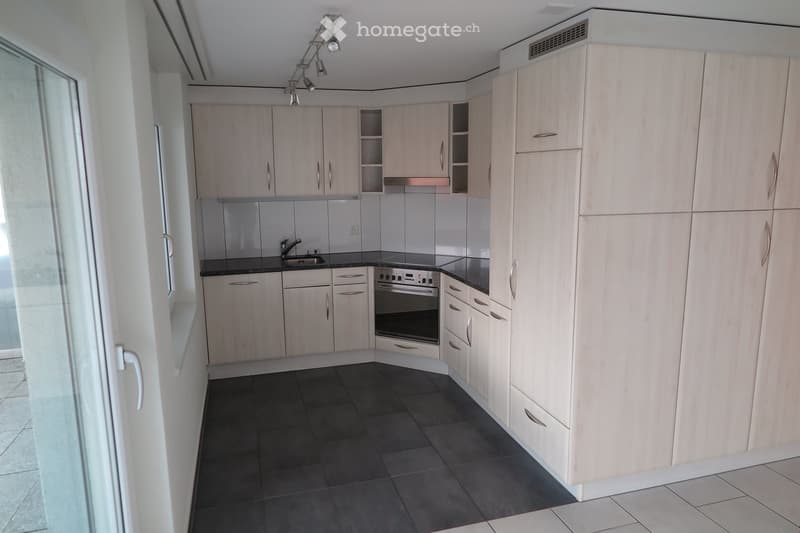 Modern kitchen with light wood cabinets, stainless steel appliances, dark countertops, and dark tiled flooring.