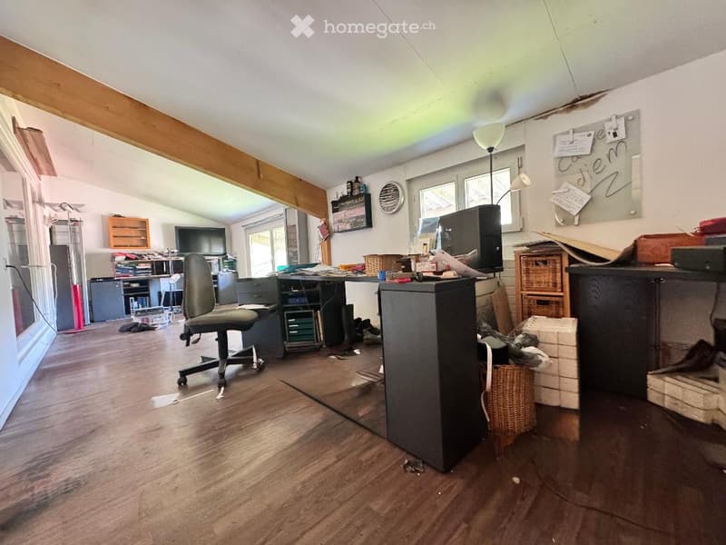 Office space with wooden flooring, large windows, desk, chair, screen, cabinets, and a lamp.