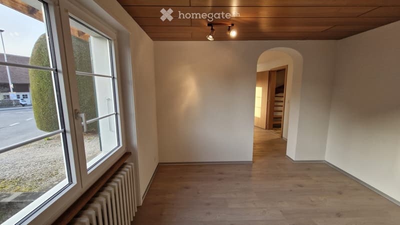 Empty hallway with wooden flooring, white walls, large windows, and a staircase leading upwards.