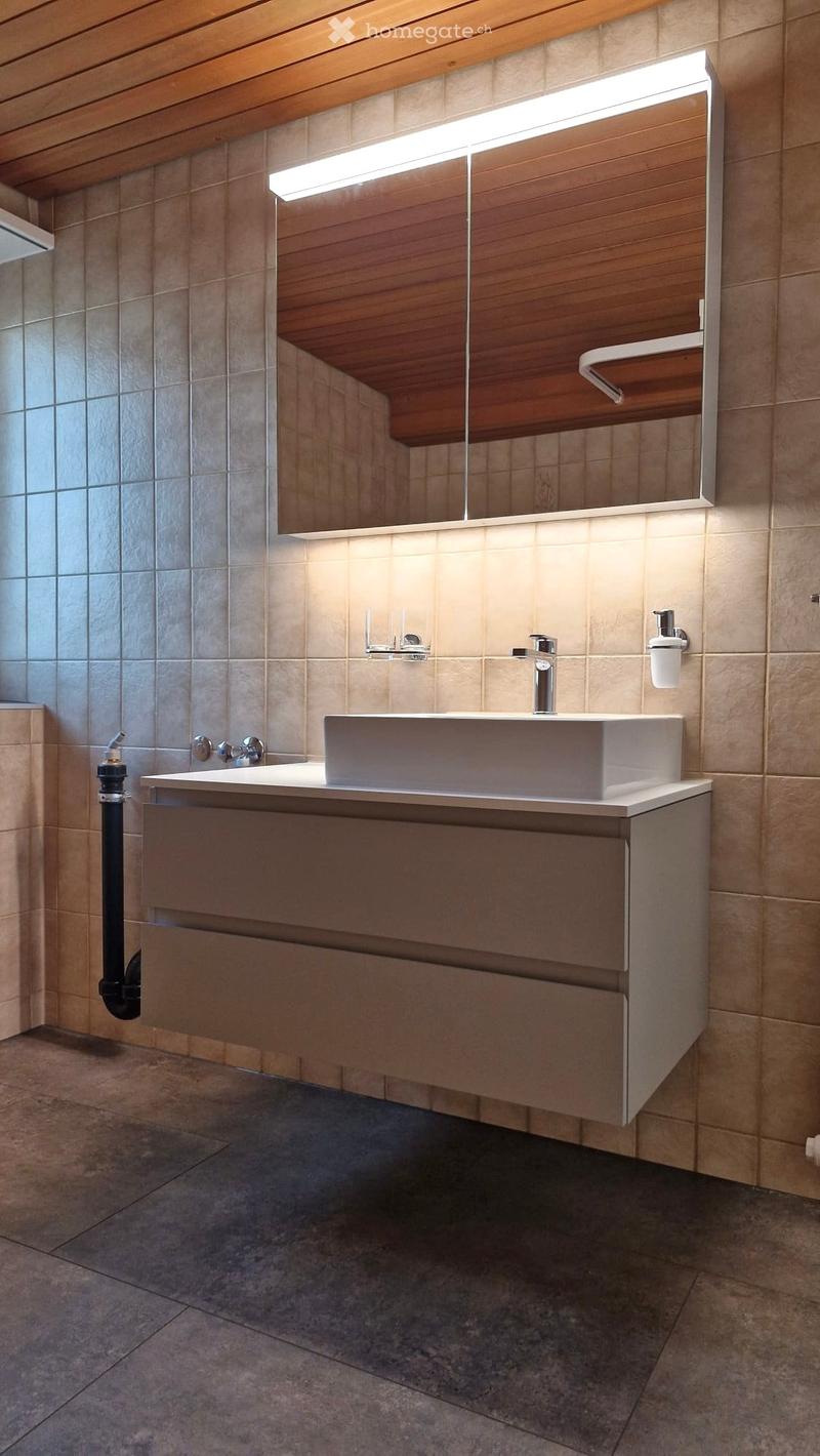 Modern bathroom with a white sink, sleek faucet, large mirror with wooden frame, and built-in cabinet.