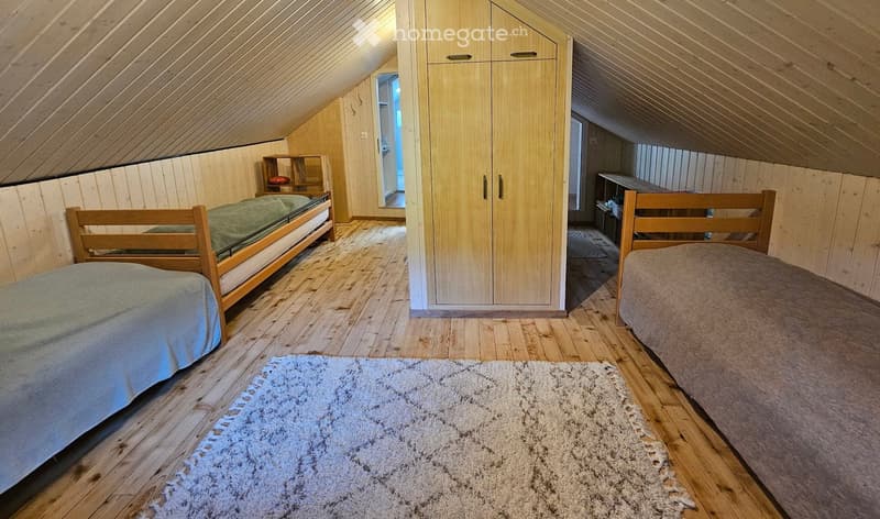 Bedroom. Cozy attic bedroom with wooden walls and slanted ceilings, featuring two single beds, a wardrobe, and a small shelf.
