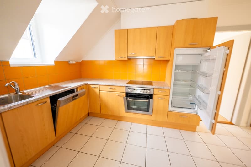 Bright kitchen with wooden cabinets, tiled floor, and modern appliances including a sink, dishwasher, oven, and refrigerator. The walls are painted in a warm orange color, and the space features a window with blinds.