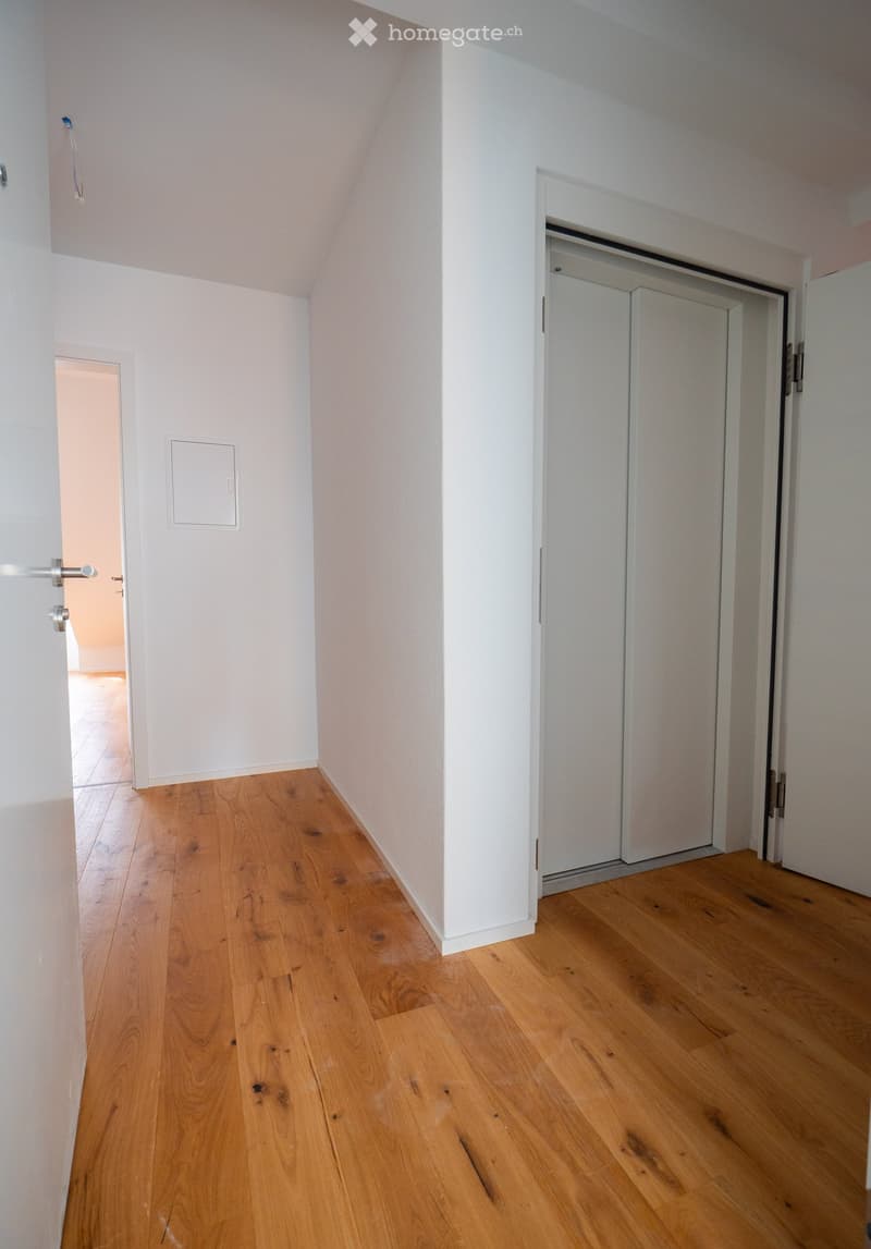 Empty hallway with light wooden flooring, white walls, and multiple doors leading to other rooms.