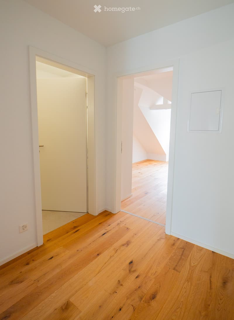 Empty room with wooden flooring and white walls, featuring two open doorways leading to adjacent spaces.