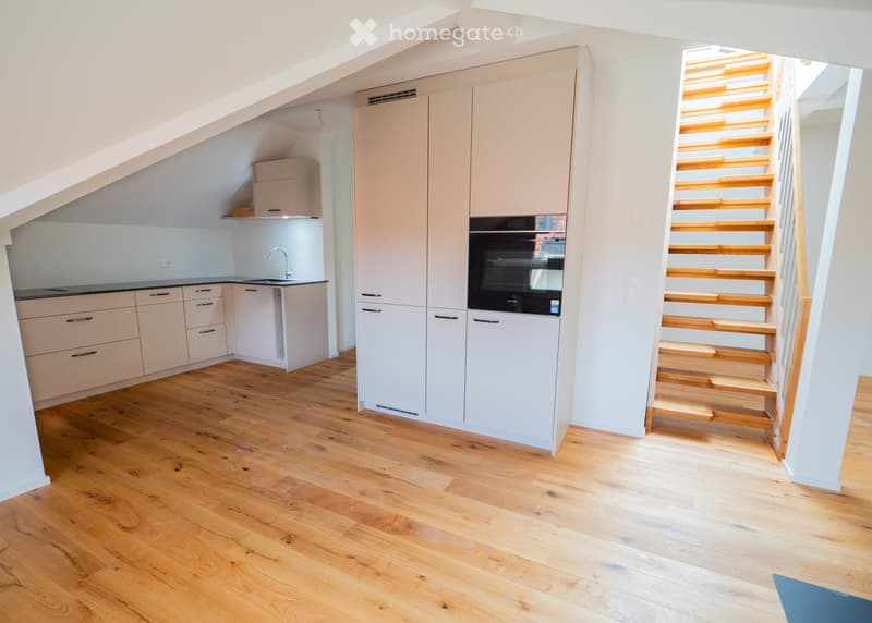 Modern kitchen with light-colored cabinets, wooden flooring, and a small staircase leading upwards.
