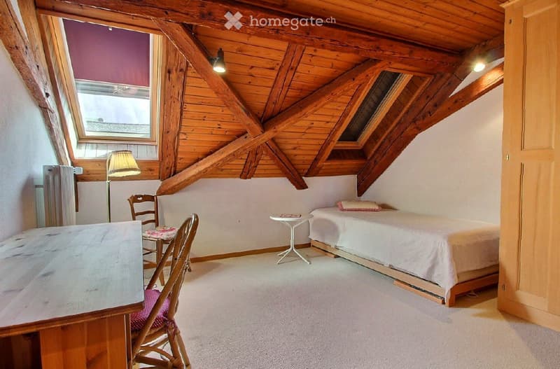 Cozy attic bedroom with wooden beams, skylight windows, a single bed, a small table, and chairs.
