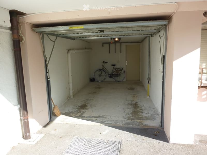 Garage with a bicycle parked inside, concrete floor, and visible pipes and storage space.