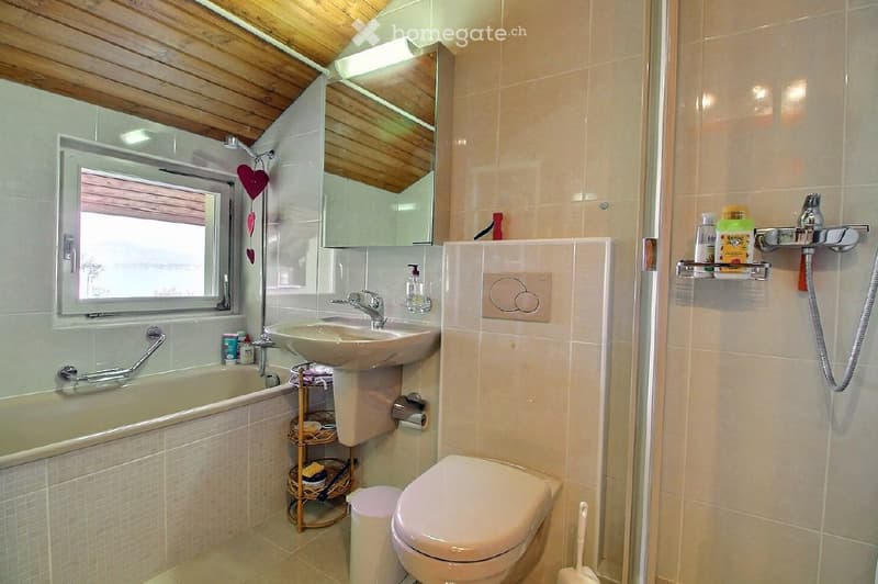 Bathroom with a bathtub, sink, toilet, mirror, and shower. Features a window, handrail, and various toiletries on shelves.