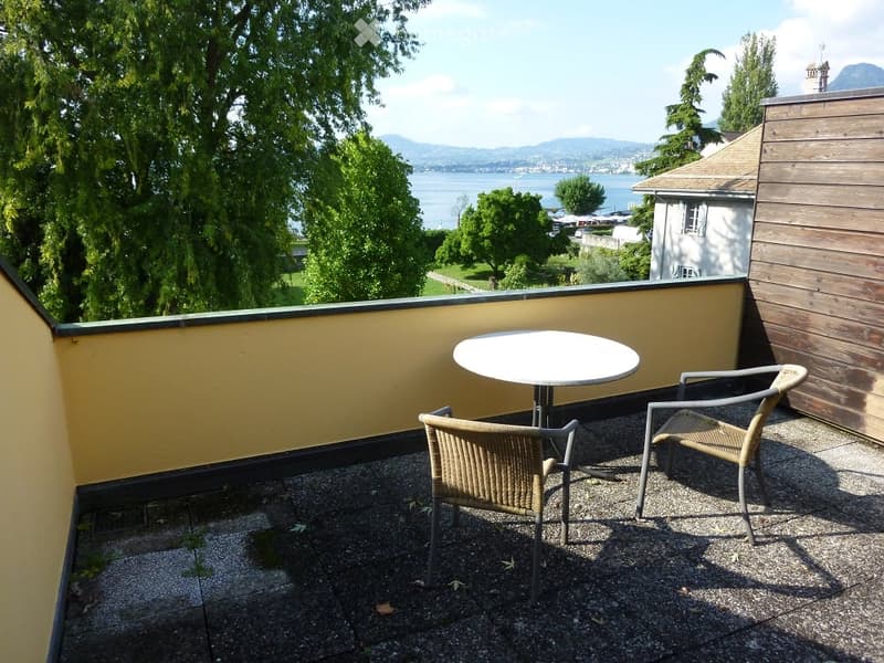 Balcony with a round table and two chairs, overlooking a scenic lake and mountains.
