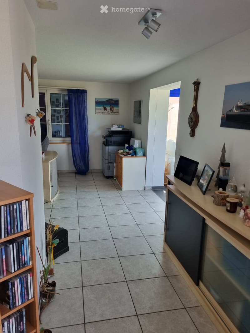 A furnished room with a tiled floor, bookshelf, small table, screen, printer, and decorative items.