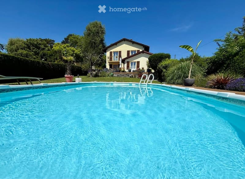 A private swimming pool in a well-maintained garden area with a house in the background, surrounded by greenery and potted plants.