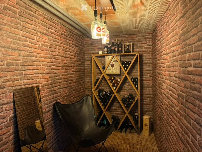 A cozy wine cellar with exposed brick walls, a wooden wine rack filled with bottles, a black leather chair, and hanging pendant lights.