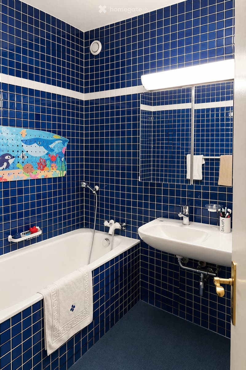 Bathroom with blue tiled walls, a white bathtub, a white sink, a mirror, and a towel on the edge of the tub.