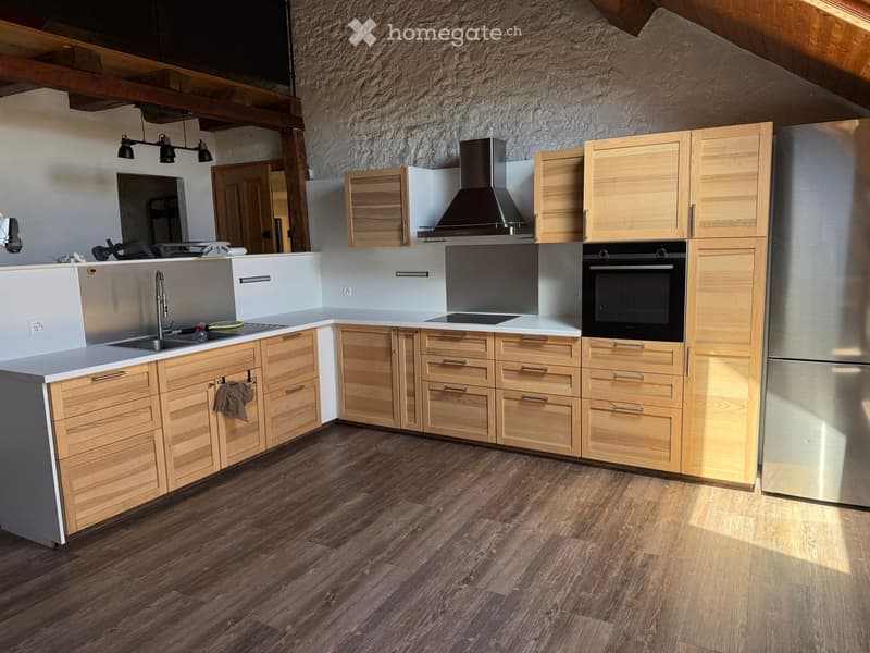 Modern kitchen with light wooden cabinets, stainless steel appliances, and a central island. Features a sink, oven, refrigerator, and range hood.