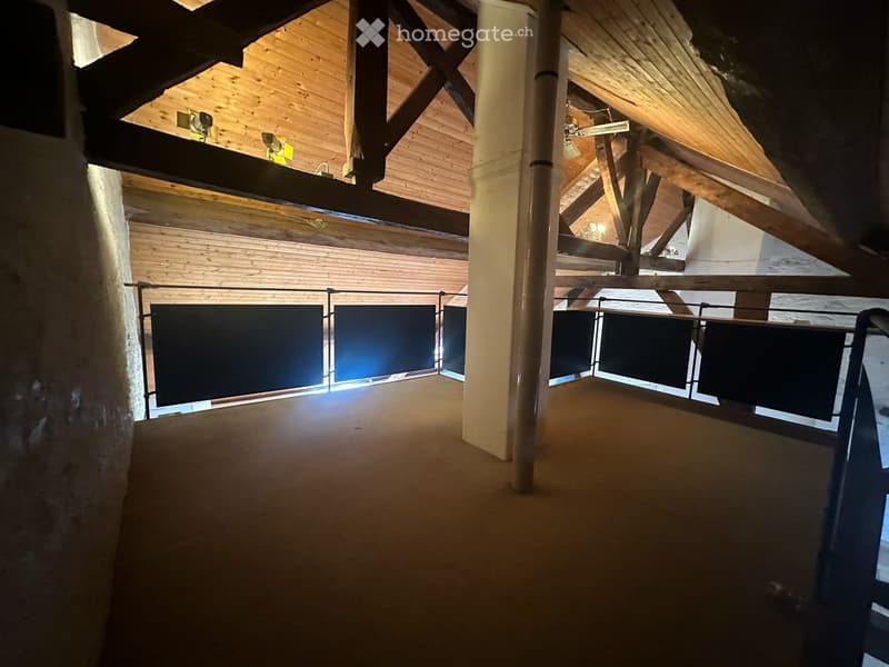 An open, spacious hallway with wooden beams and exposed wooden ceiling, featuring a metal railing and a polished concrete floor.