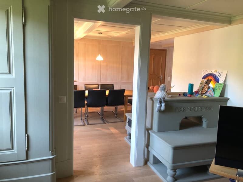 A well-lit hallway leads to a dining area with a table and chairs, and a small sitting area with a stool and decorative items.