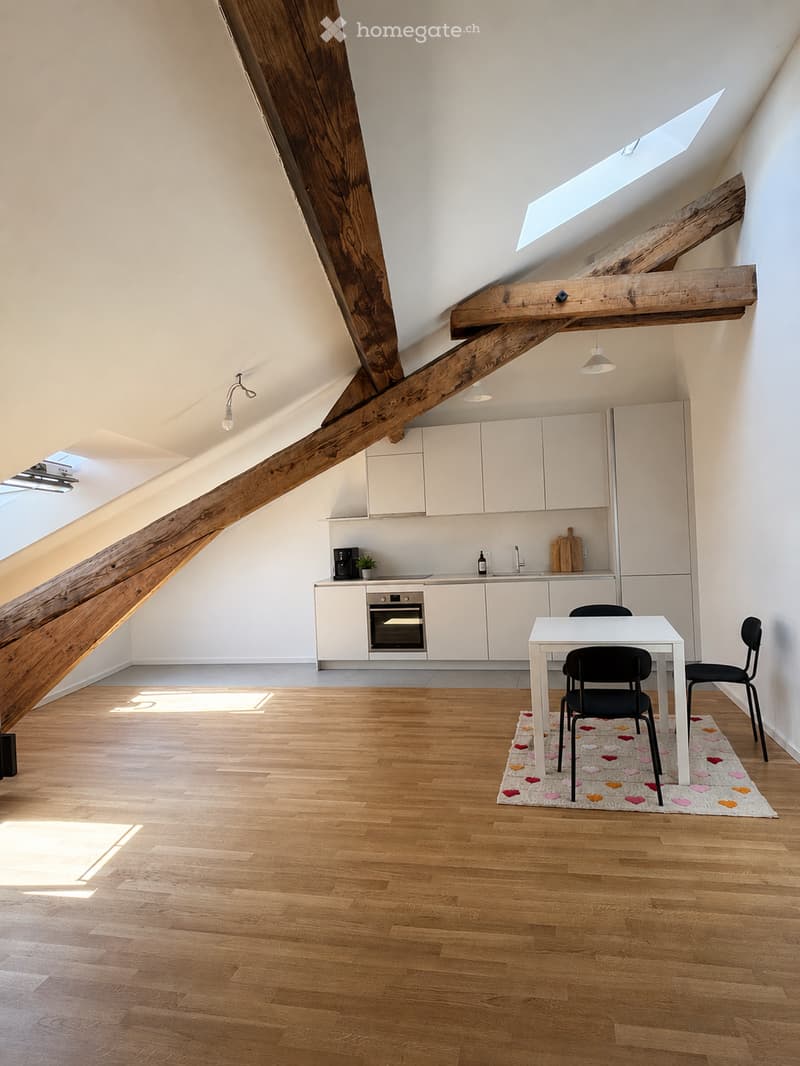 Bright, modern kitchen with white cabinets, wooden beams, and a dining area featuring a white table and black chairs on a heart-patterned rug.