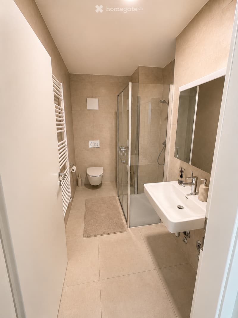 Modern bathroom with beige tiles, a white sink, a toilet, a glass-enclosed shower, and a towel rack.
