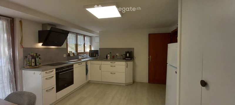 Modern kitchen with white cabinets, stainless steel appliances, and a central island. Features include a refrigerator, oven, sink, faucet, and various kitchen items on the counter.