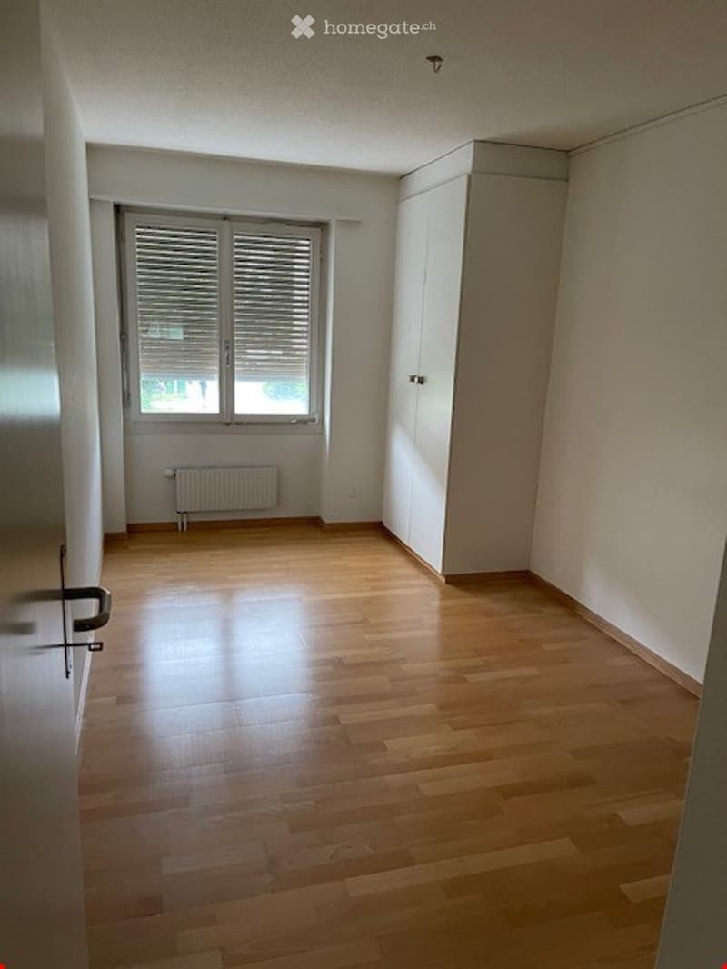 Empty room with wooden flooring, white walls, a window with blinds, and a built-in closet.