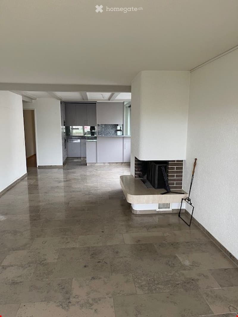 Empty living space with a fireplace, modern kitchen in the background, polished tile floor, and white walls.